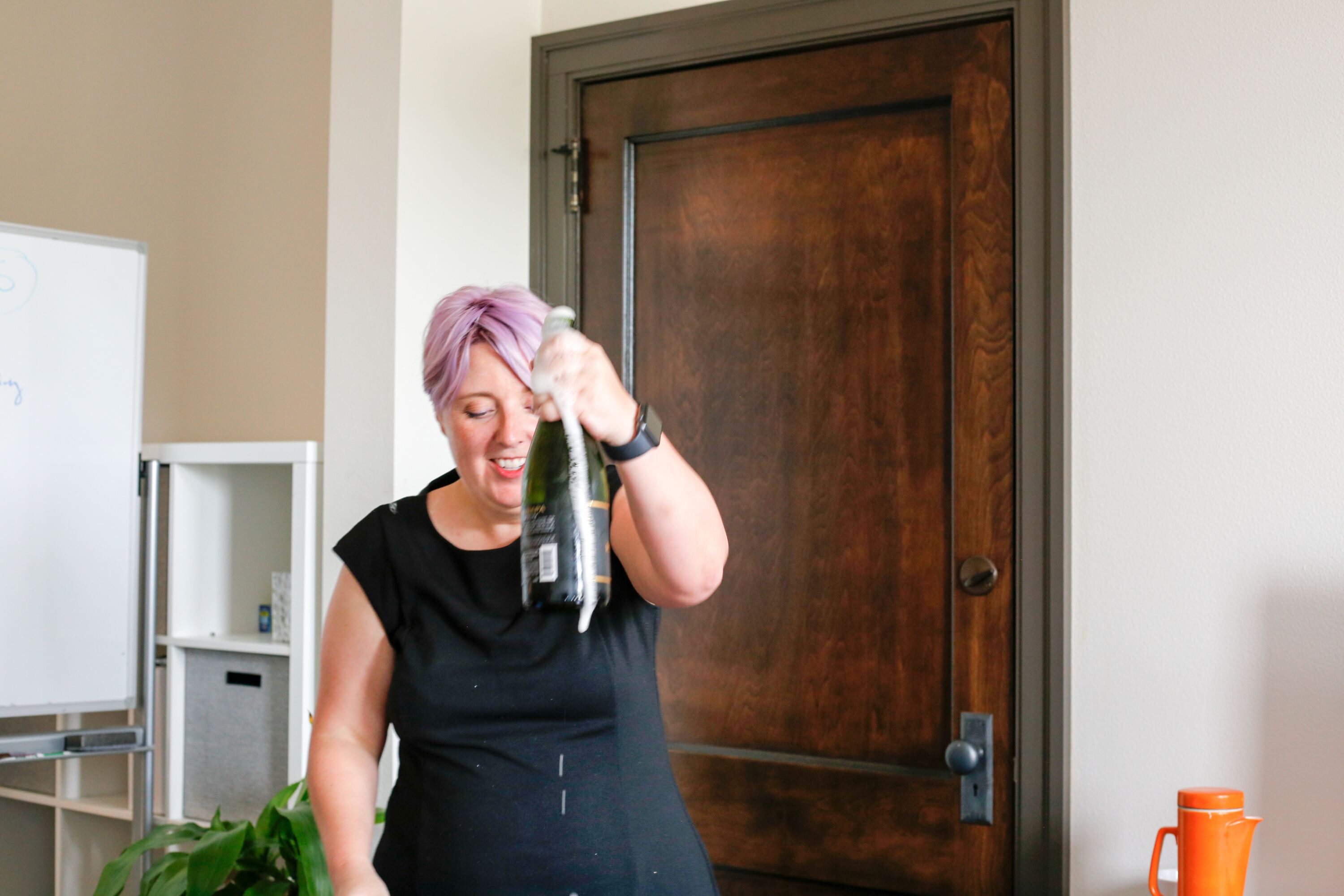 Woman with purple hair spraying champagne from a bottle.